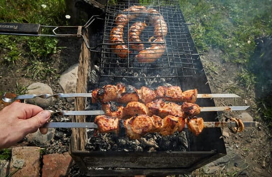 Man preparing shashlik or shish kebab over charcoal. Barbeque meat and sausages or bratwurst on a grill grate in backyard. Grilled meat on metal skewer outdoor. BBQ party or picnic food. Close up shot