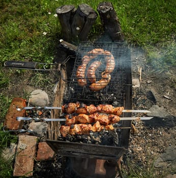 Man preparing shashlik or shish kebab over charcoal. Barbeque meat and sausages or bratwurst on a grill grate in backyard. Grilled meat on metal skewer outdoor. BBQ party or picnic food. Close up shot