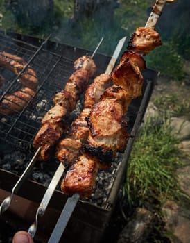 Man preparing shashlik or shish kebab over charcoal. Barbeque meat and sausages or bratwurst on a grill grate in backyard. Grilled meat on metal skewer outdoor. BBQ party or picnic food. Close up shot