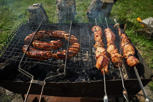 Man preparing shashlik or shish kebab over charcoal. Barbeque meat and sausages or bratwurst on a grill grate in backyard. Grilled meat on metal skewer outdoor. BBQ party or picnic food. Close up shot