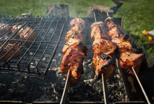 Man preparing shashlik or shish kebab over charcoal. Barbeque meat and sausages or bratwurst on a grill grate in backyard. Grilled meat on metal skewer outdoor. BBQ party or picnic food. Close up shot