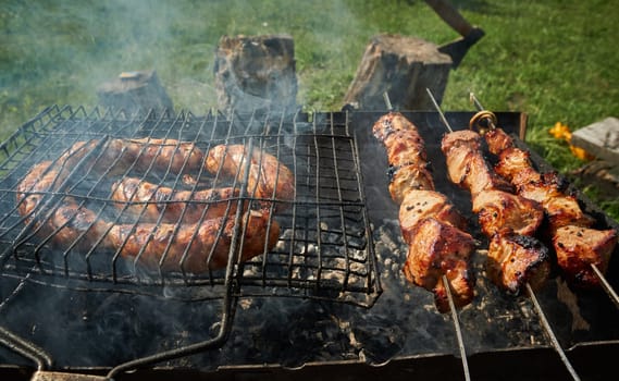 Man preparing shashlik or shish kebab over charcoal. Barbeque meat and sausages or bratwurst on a grill grate in backyard. Grilled meat on metal skewer outdoor. BBQ party or picnic food. Close up shot
