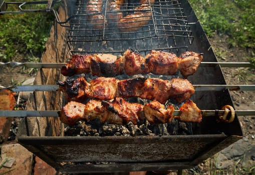 Man preparing shashlik or shish kebab over charcoal. Barbeque meat and sausages or bratwurst on a grill grate in backyard. Grilled meat on metal skewer outdoor. BBQ party or picnic food. Close up shot