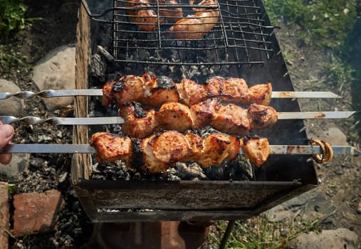 Man preparing shashlik or shish kebab over charcoal. Barbeque meat and sausages or bratwurst on a grill grate in backyard. Grilled meat on metal skewer outdoor. BBQ party or picnic food. Close up shot