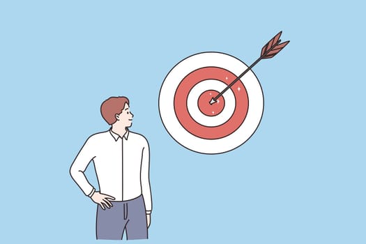 Business success, achieving goal, leadership concept. Young smiling businessman cartoon character standing looking at darts game with reached center arrow vector illustration