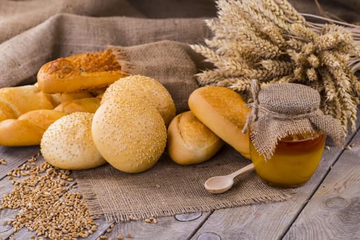 Honey in a jar, slice of bread, wheat and milk on an old vintage planked wood table from above. Rural or rustic style breakfast concept. Background layout with free text space.