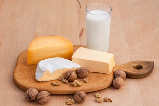 Camembert, Dutch cheese, walnuts, milk and butter on a wooden table