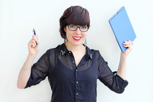 A young woman with glasses and pen and pad, happy about a passed exam