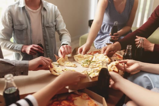 A pizza party, a group of friends chatting and happily eating pizza at the table and drinking sweet soda water. Many friends handing out together because of birthday celebration. Cheeses pizza pieces