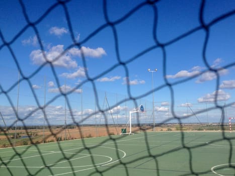 Urban multisports court seen behind safety net. Blue cloudy sky