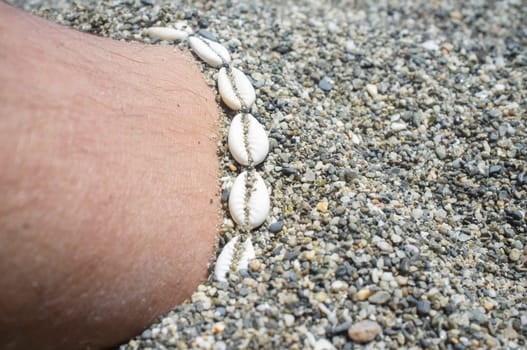 Shell ankle bracelet on half buried male leg. Symbol of summertime