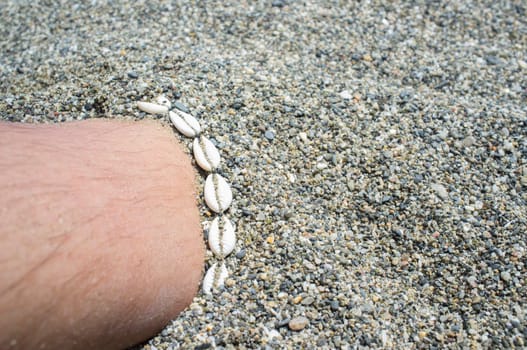 Shell ankle bracelet on half buried male leg. Symbol of summertime