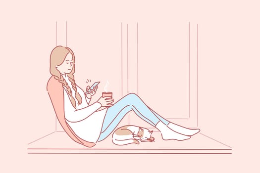 Quarantine, recreation, communication, media, coronavirus concept. Young smiling woman girl sitting on windowsill with pet cat drinking tea coffee chatting in social network. Spending time on lockdown