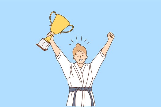 Girl karate fighter and winner concept. Smiling happy girl in white kimono with belt karate fighter standing with golden trophy in hands and celebrating victory feeling confident