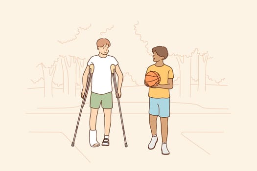 Health, care, sport, basketball, friendship concept. Young boys children african american guy holding ball and disabled friend with crutches walking together. Friendly support and rehabilitation.