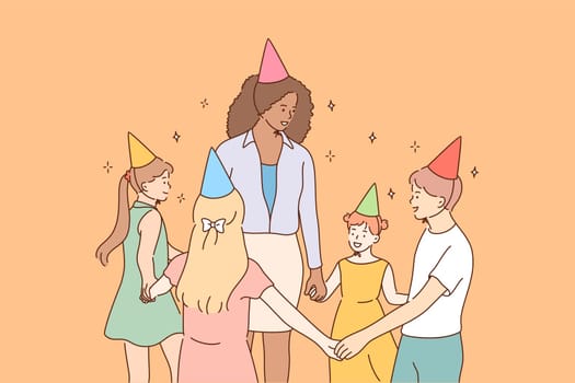 Entertainment, holiday, education, celebration, childhood concept. Young smiling african american woman teacher character leads roundelay with children kids pupils in kindergarten celebrating birthday