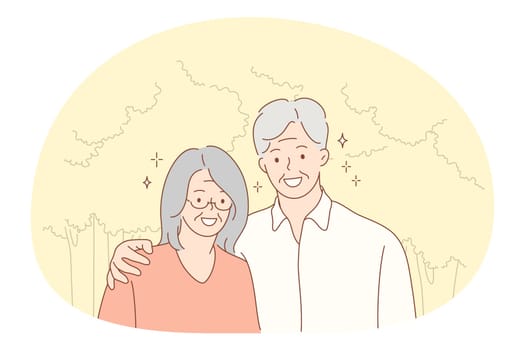 Senior elderly couple living happy active lifestyle concept. Portrait of happy mature aged couple pensioners woman and man standing hugging and looking at camera outdoors. Retiree, pensioner happiness