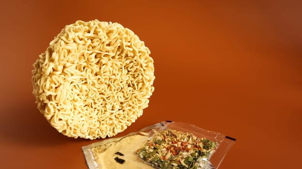 circle of instant noodles with raw spices on a plain brown background. Sprinkle dry Chinese or Korean vermicelli with salt and spices before pouring boiling water. pasta and flavors included