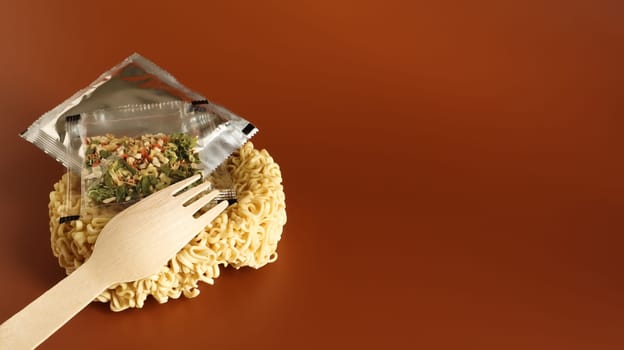 Raw instant noodles in the shape of a circle with a wooden fork and aromatic seasonings and butter. pasta, for the preparation of which it is enough to pour boiling water and wait a few minutes