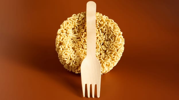 Raw instant noodles in the shape of a circle with a wooden disposable fork. pasta, for the preparation of which it is enough to pour boiling water and wait a few minutes. spaghetti. Copy space.