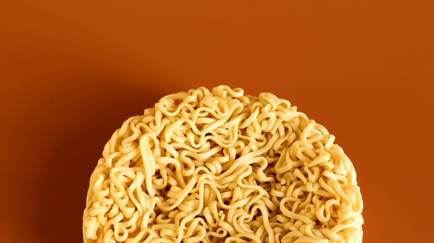 Korean instant noodles in the shape of a circle on a brown background. A yellowish-white dried raw vermicelli with long round lines and twisted in different directions into a briquette
