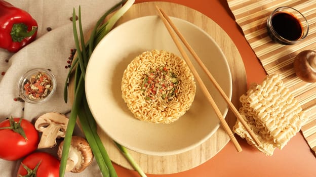 Instant noodles with king mushrooms, seasonings, soy sauce, peppers, green onions, tomatoes. Vegetable fast vegetarian soup. The process of cooking Asian food on the table. Vermicelli, spaghetti.