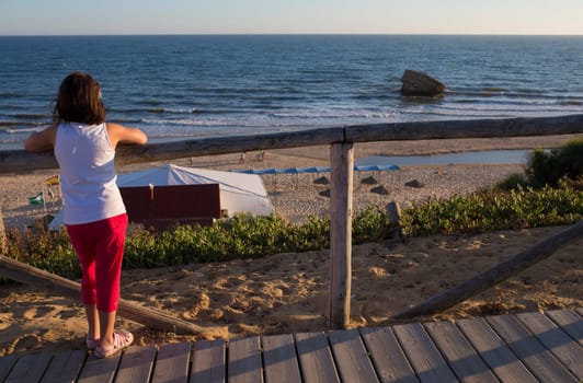 Little girl observing Donana Beach from wooden footpath. Costa de la Luz seashore, Huelva, Spain
