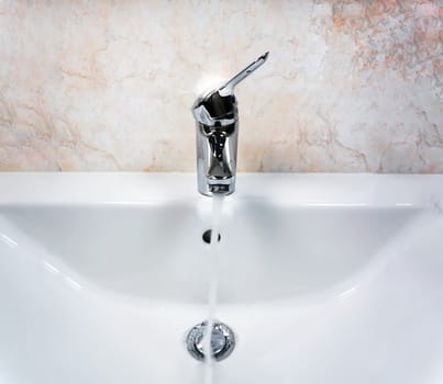 Chromed faucet with lever to mix hot and cold water on a modern white sink in a bathroom with tiled walls. Domestic life and hygiene