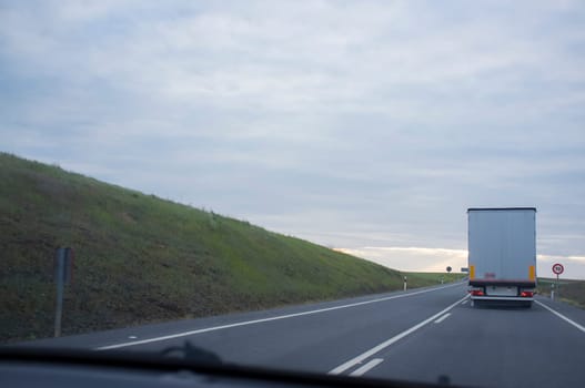 Driving behind refrigerator truck or chiller lorry at sunset. View from the inside of the car