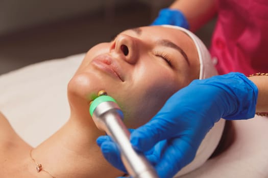 Young woman getting ultrasound skin cleansing and face treatment at beauty salon. Beautician takes care of her face.