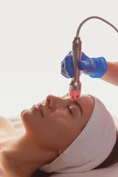 Young woman getting microcurrents skin cleansing and face treatment at beauty salon. Beautician takes care of her face