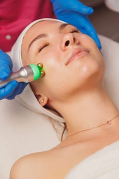 Young woman getting ultrasound skin cleansing and face treatment at beauty salon. Beautician takes care of her face.