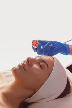 Young woman getting microcurrents skin cleansing and face treatment at beauty salon. Beautician takes care of her face
