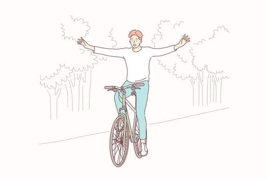 Cycling in park, freedom, lifestyle concept. Young happy smiling boy teenager student or man cyclist indulges in bicycling without hands in park. Outdoor sport activity healthy lifestyle leisure time.