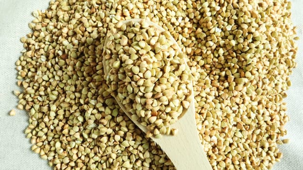 Buckwheat scattered background, raw green cereal in a wooden spoon. Healthy groats. Organic raw non-fried vegetarian food. The concept of a healthy and balanced diet. Diet product. healthy groats