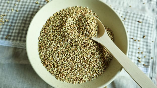 Uncooked green buckwheat in a beige plate with a wooden spoon. Great food. healthy groats. Organic raw non-fried vegetarian food. The concept of a healthy and balanced diet. Dietary foods
