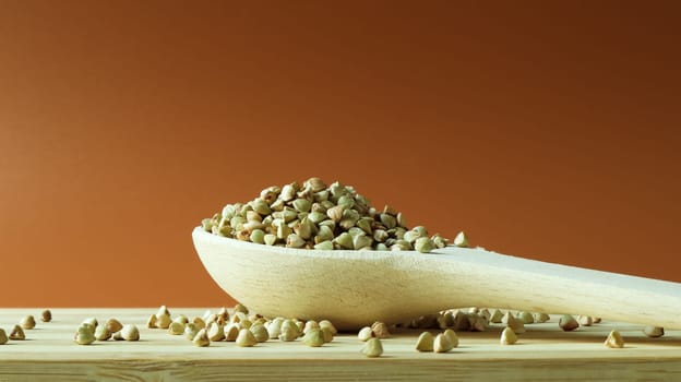 Green buckwheat in a wooden spoon on a brown background. Great food. healthy groats. Organic raw non-fried vegetarian food. The concept of a healthy and balanced diet. Dietary foods. Copy space.