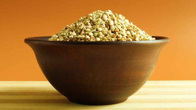 Raw green buckwheat in a brown clay plate on a brown background. Vegan organic food concept. The concept of diet, weight loss, healthy and proper nutrition. Copy space for text or logo