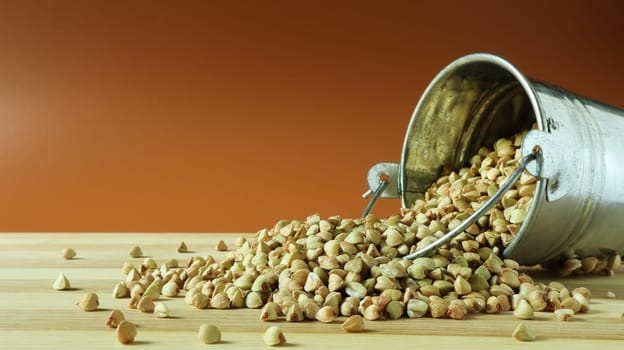 Small metal bucket with raw buckwheat on a board on a brown background. Organic vegetarian food. The concept of a healthy and balanced diet. Dietary nutrition. Copy space.