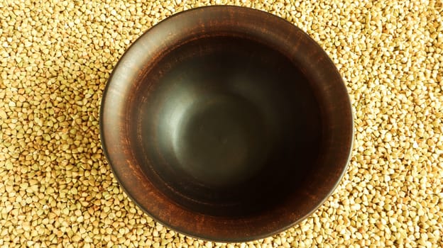 Raw green buckwheat in a brown clay plate on a brown background. Vegan organic food concept. The concept of diet, weight loss, healthy and proper nutrition. Copy space for text. Top view, flat lay.