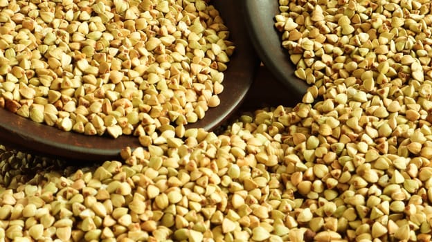 Buckwheat scattered background, raw green buckwheat in a brown clay bowl or plate. Healthy groats. Organic raw non-fried vegetarian food. The concept of a healthy and balanced diet. Diet food.