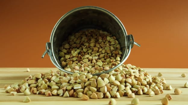 Small metal bucket with raw buckwheat on a board on a brown background. Organic vegetarian food. The concept of a healthy and balanced diet. Dietary nutrition. Copy space.