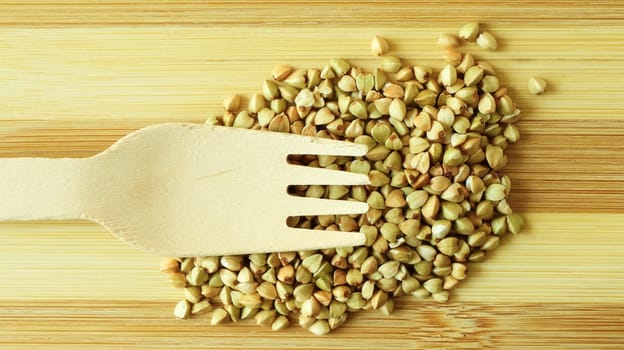 Raw green organic buckwheat on a wooden background with a wooden fork. Dietary nutrition. Copy space Concept of vegetarianism, balanced and healthy diet