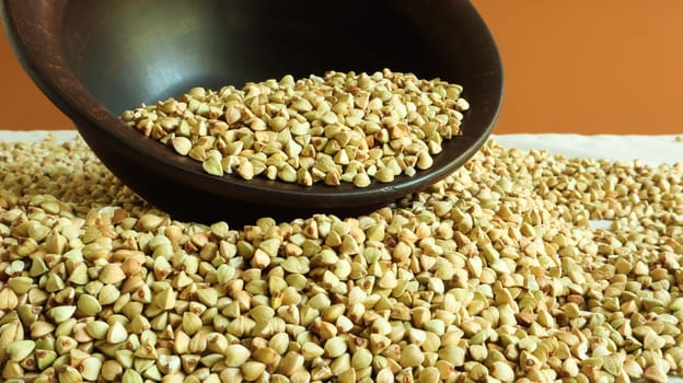 Buckwheat scattered background, raw green buckwheat in a brown clay bowl or plate. Healthy groats. Organic raw non-fried vegetarian food. The concept of a healthy and balanced diet. Diet food.