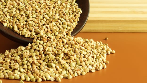 Buckwheat scattered background, raw green buckwheat in a brown clay bowl or plate. Healthy groats. Organic raw non-fried vegetarian food. The concept of a healthy and balanced diet. Diet food.