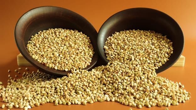 Buckwheat scattered background, raw green buckwheat in a brown clay bowl or plate. Healthy groats. Organic raw non-fried vegetarian food. The concept of a healthy and balanced diet. Diet food.