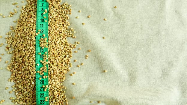 Green measuring tape on a background of raw buckwheat in a dish, concept of diet and healthy nutrition. Vegan organic food concept. Quarantine weight loss. Copy space for text. Top view, flat lay.