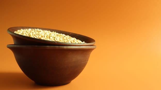 Raw green buckwheat in a brown clay plate on a brown background. Vegan organic food concept. The concept of diet, weight loss, healthy and proper nutrition. Copy space for text or logo