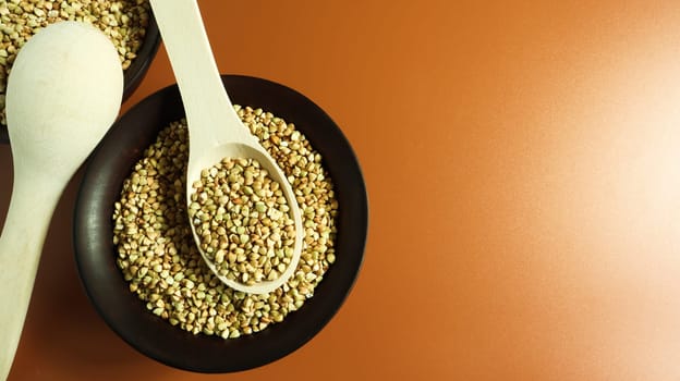 Raw green buckwheat in a brown clay plate and a wooden spoon. Vegan organic food concept. The concept of diet, weight loss, healthy and proper nutrition. Copy space for text. Top view, flat lay.
