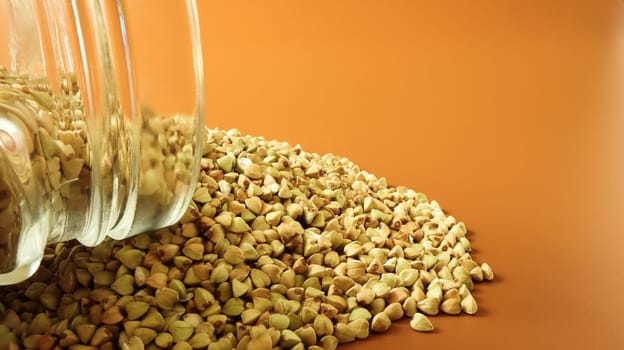 Scattered raw green buckwheat with a glass jar for cereals. Vegan organic food concept. The concept of diet, weight loss, healthy and proper nutrition. Triangle shaped scatter kernels.